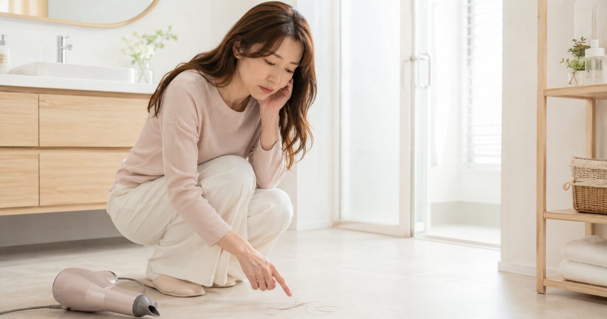 洗面所でドライヤー後に落ちた抜け毛の量を心配する女性
